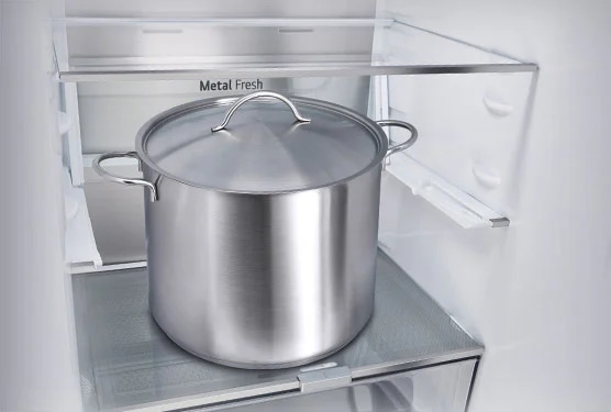 냉장고 내부에 큰 스테인리스 스틸 냄비가 놓여 있습니다. 냉장고 선반에 ""Metal Fresh""라는 텍스트가 적혀 있습니다. 냄비는 뚜껑이 닫혀 있으며 손잡이가 양쪽에 달려 있습니다. 냉장고 내부는 깔끔하고 현대적인 디자인입니다.