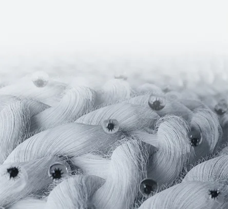 옅은 회색 배경 위에 흰색 섬유들이 서로 엮여 있는 모습이 보입니다. 섬유 사이사이에 작은 물방울들이 맺혀 있으며, 이 물방울들은 빛을 반사하여 반짝이는 효과를 나타내고 있습니다. 섬유의 질감과 물방울의 배치가 강조된 이미지입니다.