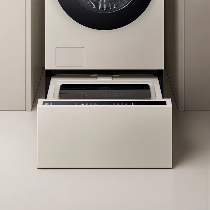 LG 트롬 오브제컬렉션 미니워시 제품이 중앙에 위치해 있으며, 상단에는 메인 세탁기의 하단부가 보이고 하단에는 미니워시의 서랍식 도어가 열려 있습니다. 제품은 베이지 색상으로, 도어 위에는 다양한 세탁 옵션을 선택할 수 있는 터치 패널이 있습니다. 미니워시는 주변의 다른 가구와 조화를 이루며 깔끔하게 설치되어 있습니다.